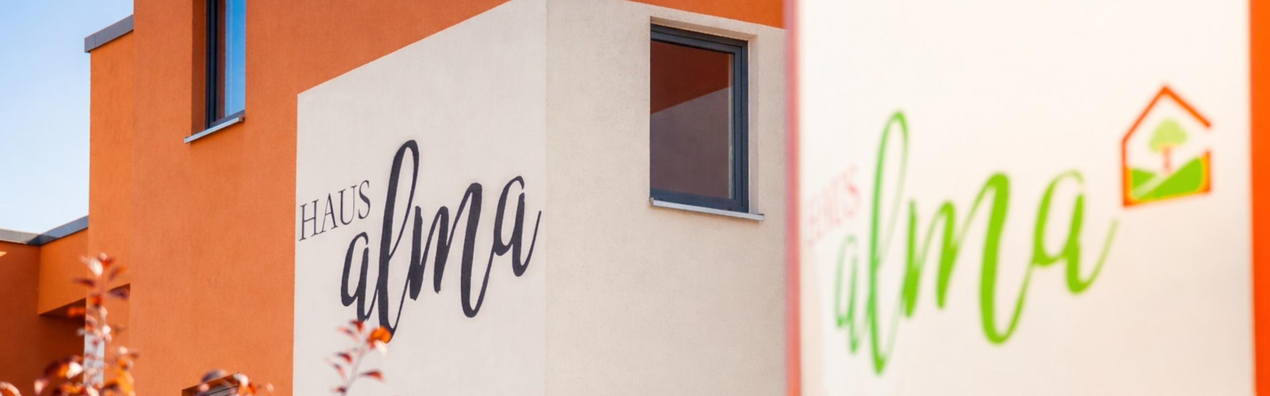 Detailauschnitt eines weiß orangenem Hauses mit der Aufschrift Haus Alma